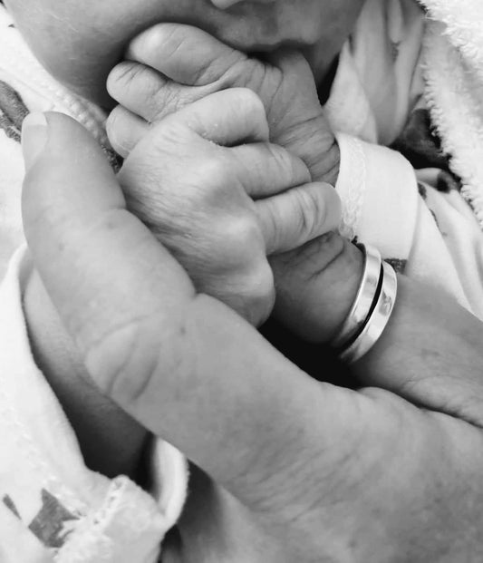 zwart wit afbeelding van babyhandje wat wat duim met ring van vrouw vasthoudt 