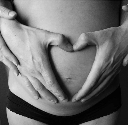 zwart wit afbeelding van zwangere buik met handen van vader in de vorm van een hartje
