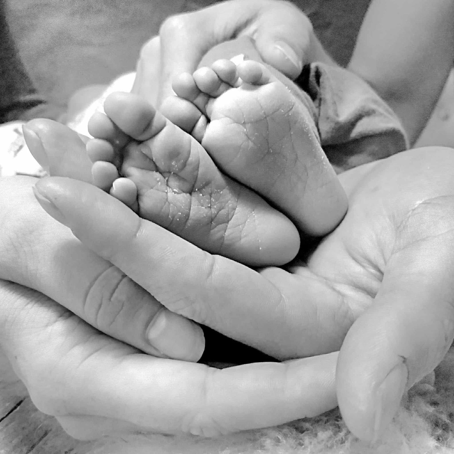 zwart wit afbeelding met handen van vader en moeder met babyvoetjes